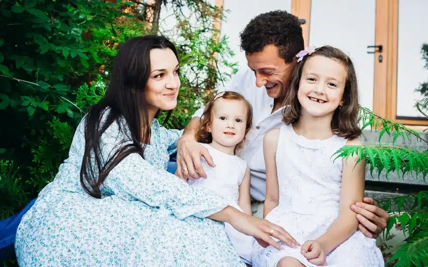 Brunette woman hugging her daughters, smiling family outdoors, emphasizing togetherness and joy, relevant to Child Tax Credit discussions.