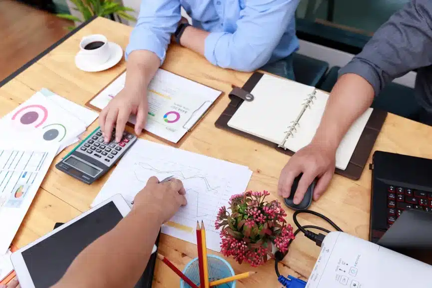 Hands analyzing financial documents and charts on a desk, with a calculator, tablet, and coffee cup, emphasizing construction accounting and tax preparation.